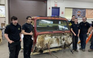 Diesel students stand next to a car part.
