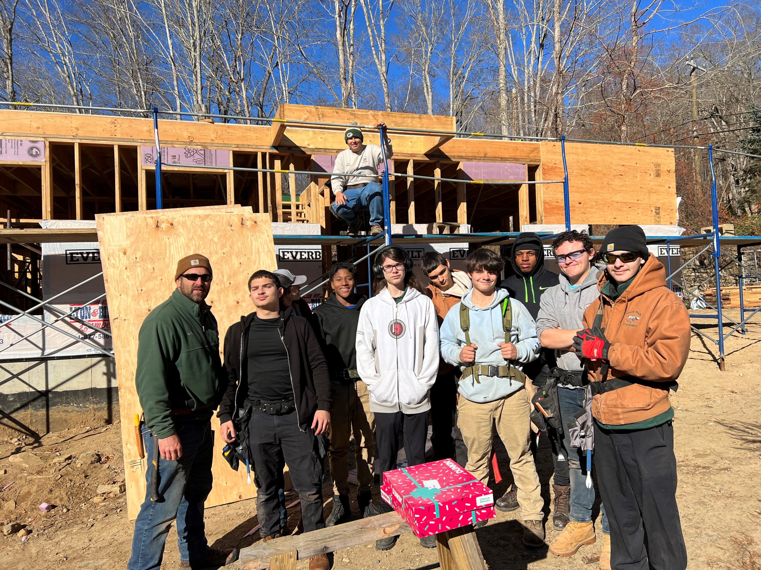 Carpentry students pose for a photo in front of the house that they are building on site.