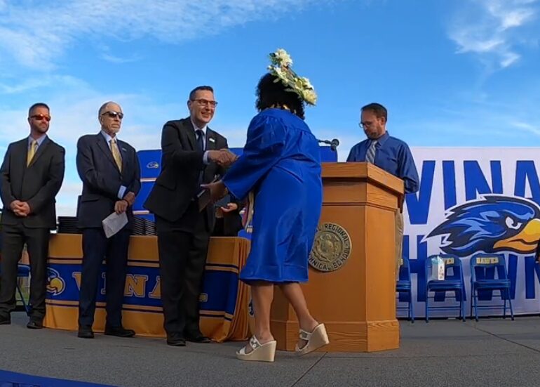 Student shakes hand with Dr. Rivera on graduation stage.